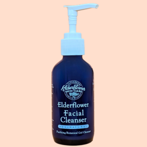 Blue glass facial cleanser bottle with a light blue pump top, labeled 'Elderflower Facial Cleanser' against a peach background.
